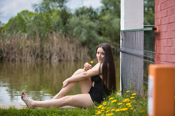 Young, dark and beautiful woman dressed in black holds in her hand a yellow flower and is happily...