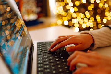 Close-up of hands typing on a laptop while sitting at a table in a cozy room. The hands of a young...