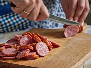 A Person in an Apron Slicing Smoked Sausage on a Wooden Cutting Board