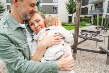 Parents embracing child outdoors at playground on a summer day