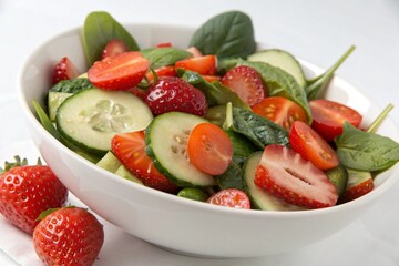 A bowl of salad with tomatoes, cucumbers, and strawberries