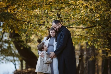 Pregnant family embracing outdoors during autumn season