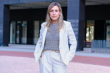 Confident businesswoman wearing a light suit and looking seriously at the camera, standing outdoors...