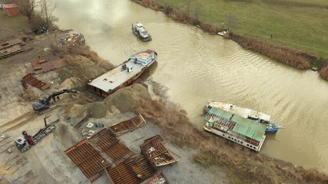 Above view on workers as cutting parts of old large vessel into smaller pieces, barge, dismantling ship, cut out rusty metal for scarp, excavator and tow truck are pull out part of old vessel's bed