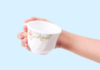 Hand holding elegant floral patterned teacup on light blue background.