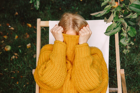 Woman hiding face in yellow sweater while resting outdoors in autumn