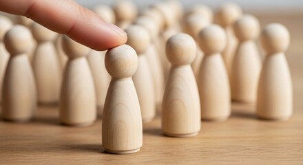 Close-up of hand selecting wooden peg doll from group — recruitment, leadership, and individual choice concept.