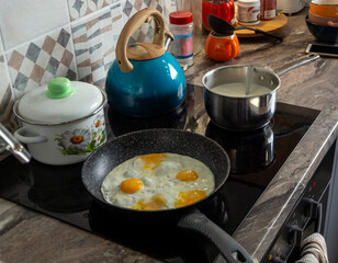 On the hob there is a frying pan with scrambled eggs, a kettle, a saucepan, and milk porridge is being cooked. Cooking food at home in the kitchen.