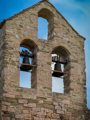A close-up of a weathered, ancient stone bell tower featuring two dark bronze bells framed by...