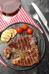 Delicious grilled beef steak with rosemary, zucchini and tomatoes served on dark textured table, flat lay