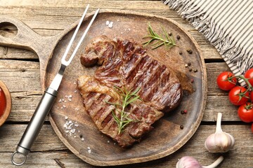 Delicious grilled beef steak with rosemary, spices, carving fork and products on wooden table, flat lay
