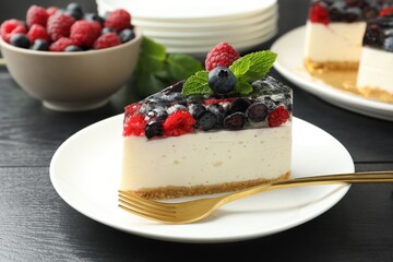 Piece of delicious cheesecake with berries and mint on black wooden table, closeup