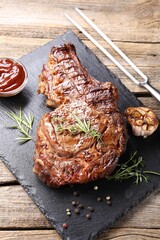 Delicious grilled beef steak with herbs, spices, ketchup and carving fork on wooden table, above view