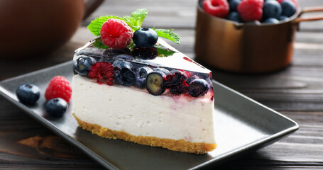 Piece of delicious cheesecake with berries and mint on wooden table, closeup