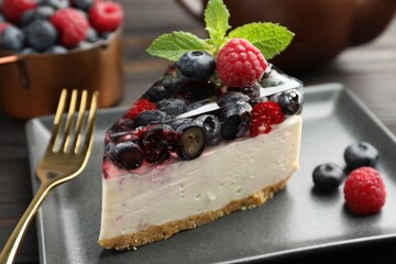 Piece of delicious cheesecake with berries, mint and fork on table, closeup