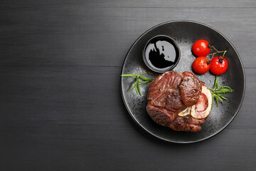 Tasty grilled beef steak served with rosemary, sauce and tomatoes on black wooden table, top view. Space for text