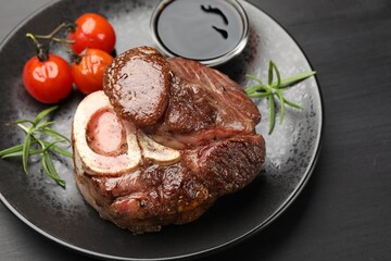 Tasty grilled beef steak served with rosemary, sauce and tomatoes on black wooden table, closeup