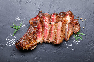 Tasty cut beef steak, salt, peppercorns and rosemary on black table, flat lay