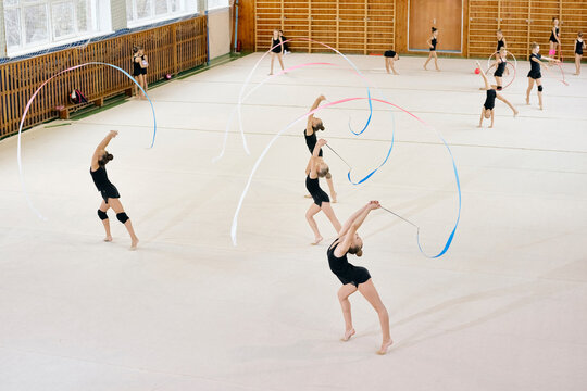 Group of Caucasian teenage girls performing rhythmic gymnastics routine with ribbons on gymnasium floor, demonstrating synchronized movements and athletic flexibility during practice - Powered by Adobe
