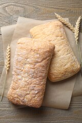 Freshly baked ciabattas and wheat ears on wooden table, flat lay