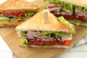 Tasty sandwiches with ham and vegetables on white wooden table, closeup