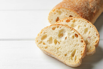 Cut crispy ciabatta on white wooden table, closeup. Space for text