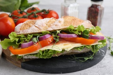 Delicious ciabatta sandwich with prosciutto, cheese and vegetables on light table, closeup