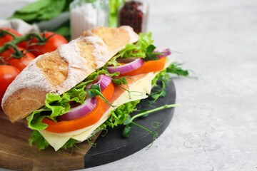 Delicious ciabatta sandwich with prosciutto, cheese and vegetables on light table, closeup. Space for text