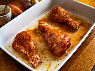 Raw seasoned chicken drumsticks in baking dish on wooden table	