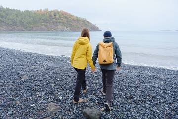Couple enjoys Turkish coastline. Sitting on stones, watching sea waves, relaxing together, slow romantic moment near calm blue water under soft winter light.