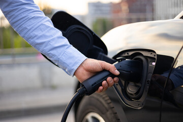 A person plugging an electric vehicle charger into a black car, promoting sustainable transportation.