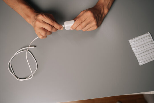 Top view of unrecognizable man connecting USB cable to electronic cigarette charger on gray desk, showcasing charging process of vaping device. Concept of modern alternative to traditional smoking.