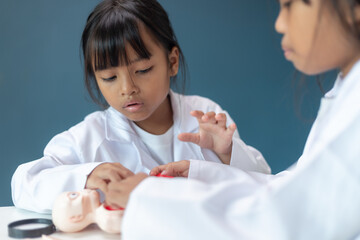 Obraz premium Two Asian children in doctor coats playing and learning with a toy patient, concept of STEM education, teamwork, healthcare learning, and child development through play at home
