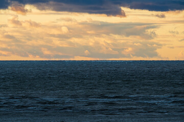 Obraz premium A dramatic sunset sky with golden clouds hangs over the dark, choppy and restless waters of the Baltic Sea.