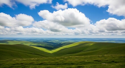 Obraz premium A vast, breathtaking landscape of rolling green hills and valleys under a dramatic blue sky with fluffy white cumulus clouds, capturing the sheer beauty of the open countryside.