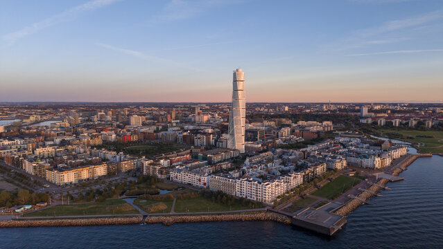 Aerial view of the Turning Torso skyscraper piercing the skyline amidst the residential and commercial buildings bathed in the warm glow of the setting sun, Nyhamnen, Malmo, Sweden.