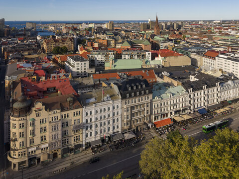 Aerial view of historic buildings with red and green roofs nestled near Gustav Adolfs torg, contrasting against the distant blue sea, Malmo, Sweden.