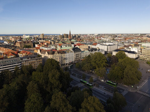 Aerial view of the city skyline with the spire of St. Peter's Church punctuating the horizon, and lush green trees lining Gustav Adolfs torg, Malmo, Sweden.