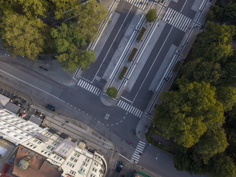 Aerial view of the stark white crosswalks cutting through the grey pavement of Gustav Adolfs torg, bordered by the lush green trees and the corner of a building, Malmo, Sweden.