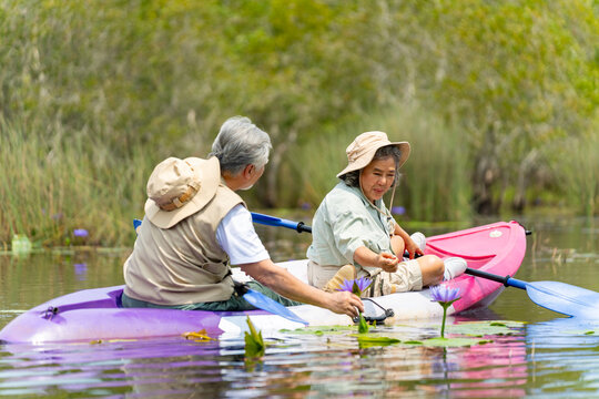 Happy Asian senior couple kayaking in the river on summer holiday vacation. Healthy retired elderly people enjoy and fun outdoor active lifestyle travel nature, sport and rowing a boat in the lake.