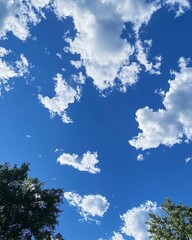 Bright blue sky dotted with fluffy white clouds. Trees are visible at the bottom