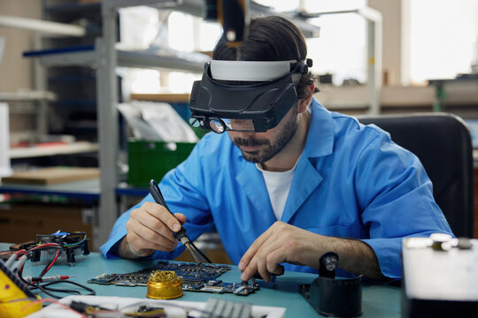 A man worker, wearing glasses is actively working on a motherboard