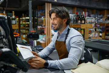 A man in apron diligently works in a local grocery store at the cash register