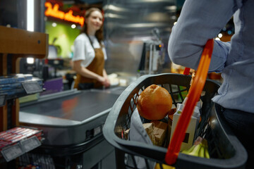 Closeup of man carrying a shopping basket full of groceries to the checkout in a store