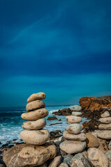 Balanced stone cairns on a rocky beach with the ocean and sky in the background, symbolizing balance and peace.
