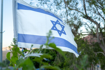 The Israeli flag flutters gently in a tree-lined area, symbolizing national pride during efforts for the liberation of hostages. This moment captures hope and solidarity in Israel.