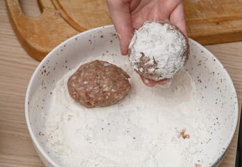 A cook breading ground pork and beef cutlets in flour before baking.