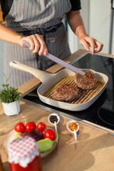 Woman cooking hamburgers in modern kitchen using grill pan
