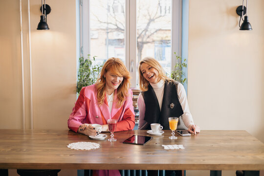 Two businesswomen laughing while having breakfast in cafe - Powered by Adobe