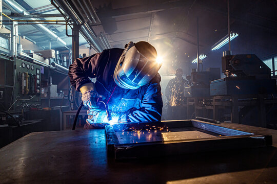 Industrial worker welding metal frame in factory workshop - Powered by Adobe